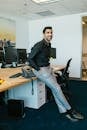 An adult man in a modern office, leaning on a desk and smiling confidently.